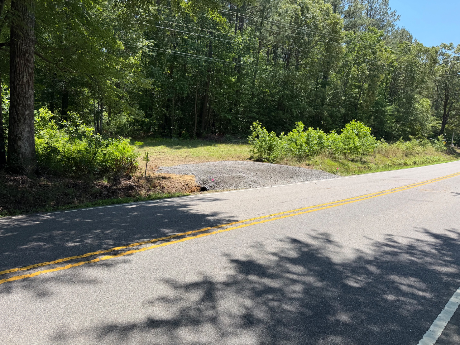 Fresh gravel road entrance with installed culvert pipe beside a roadside tree line